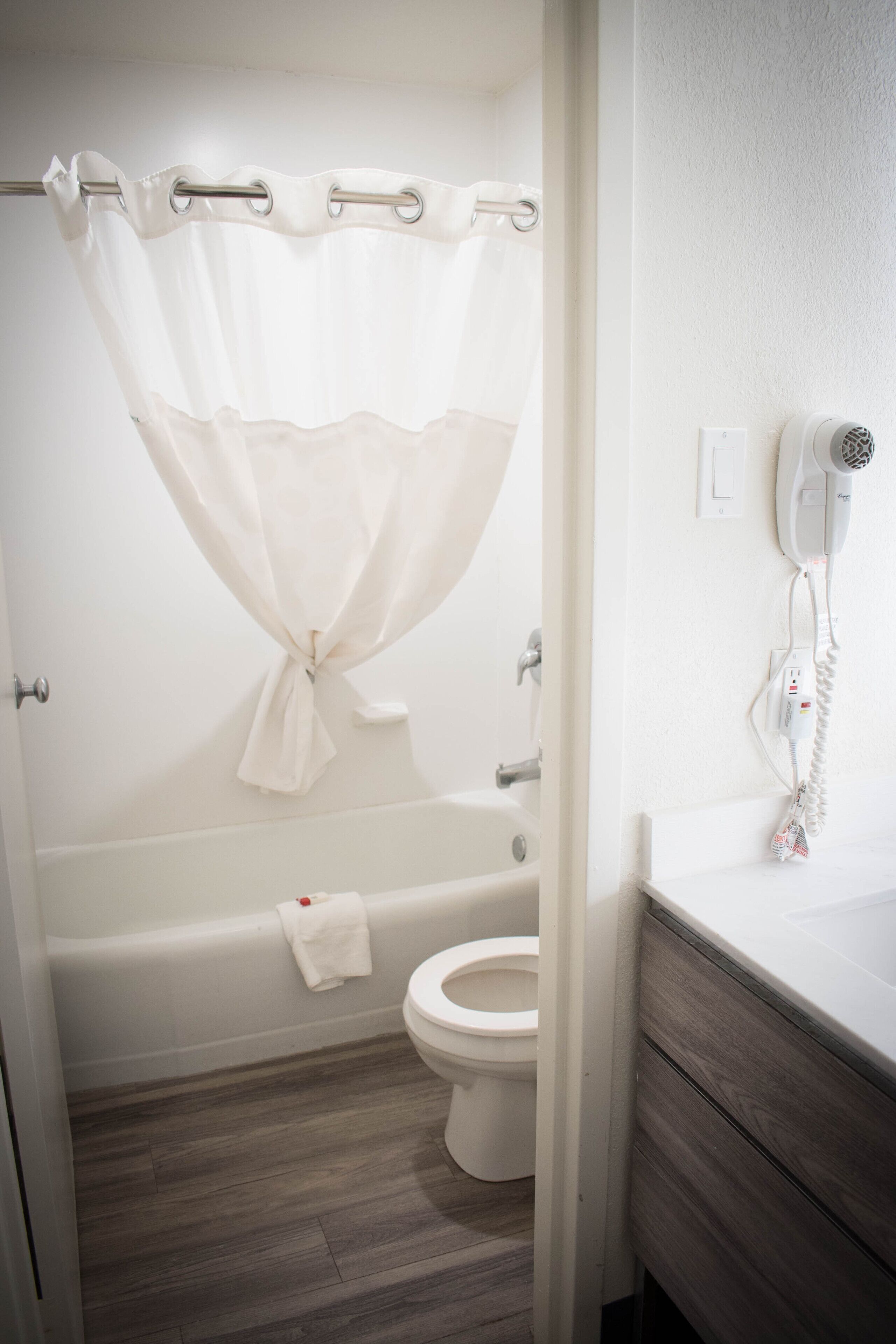 A bathroom with a bathtub, toilet, and a hairdryer on the wall.