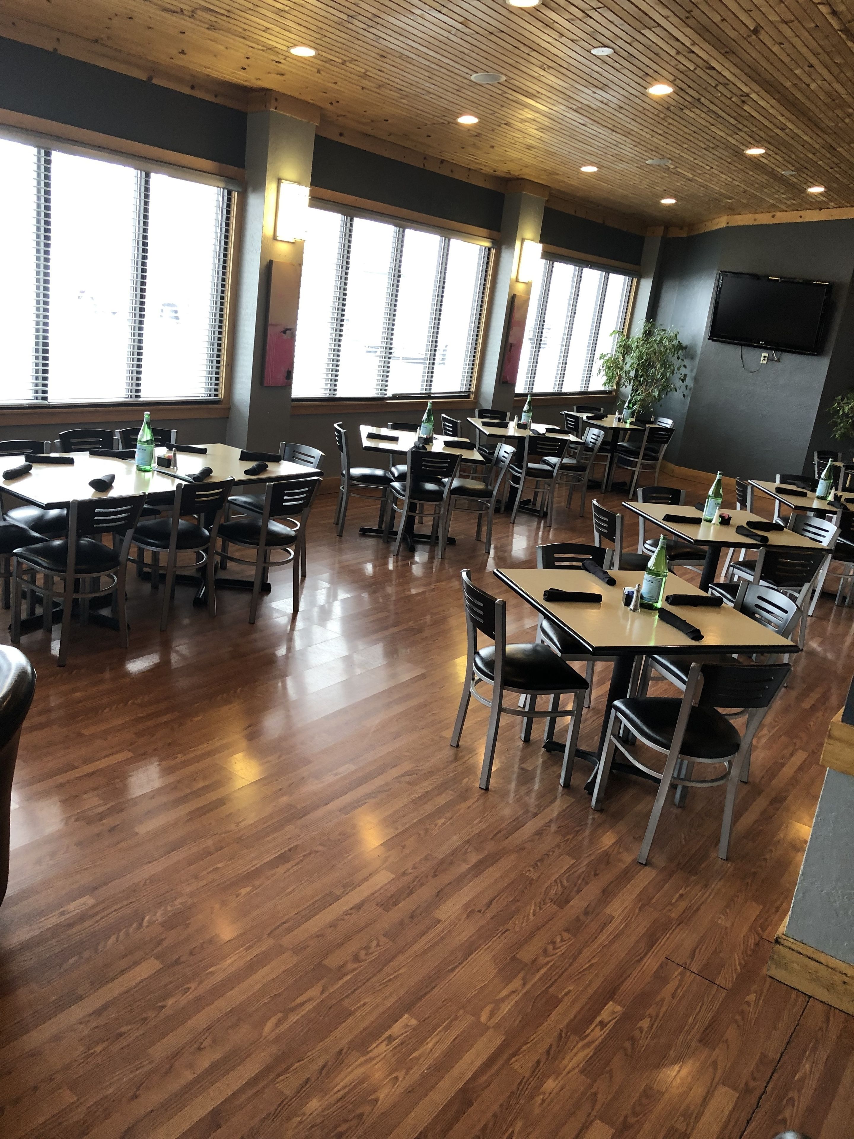 Un comedor amplio con varias mesas y sillas, ventanas grandes con persianas y techo de madera.