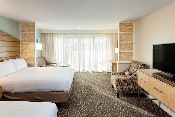 Une chambre d’hôtel avec un grand lit, un bureau, une télévision et un fauteuil à motifs.