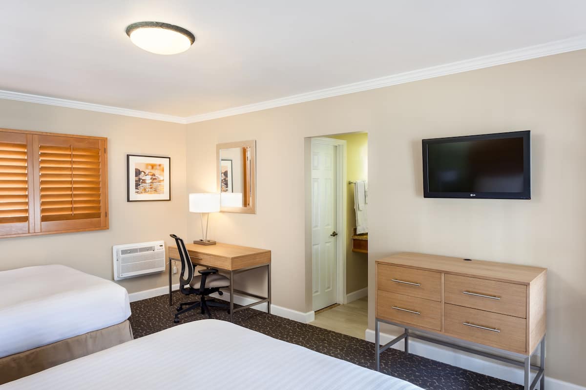 Habitación de hotel con dos camas, un escritorio con silla, cómoda, televisor y puerta que da a un baño.