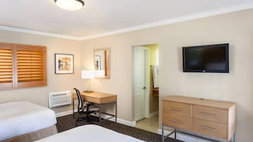 Ett hotellrum med två sängar, ett skrivbord med en stol, en byrå, en tv och en dörr som leder till ett badrum.
