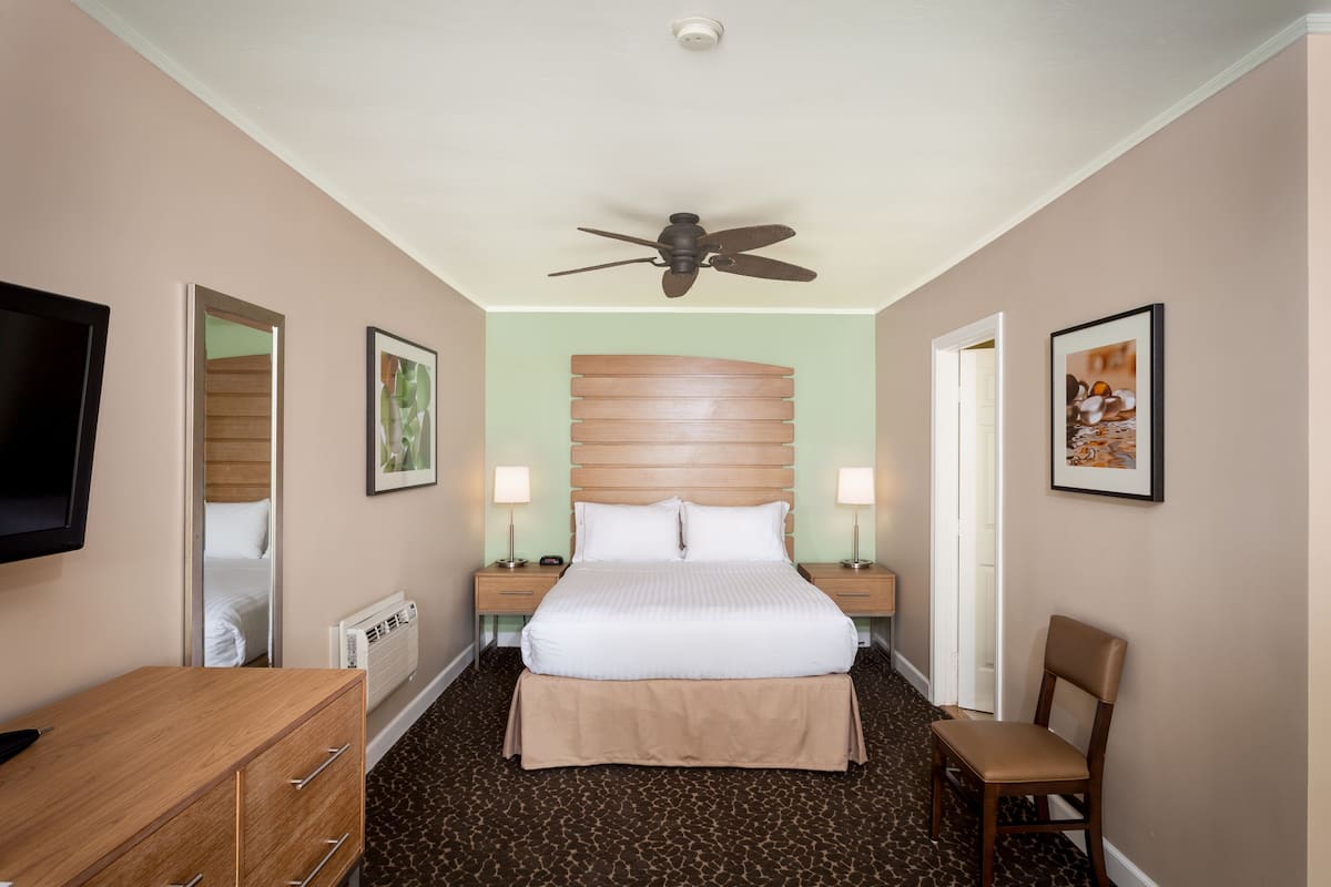 Habitación de hotel con cama, escritorio, silla, televisor y ventilador de techo.