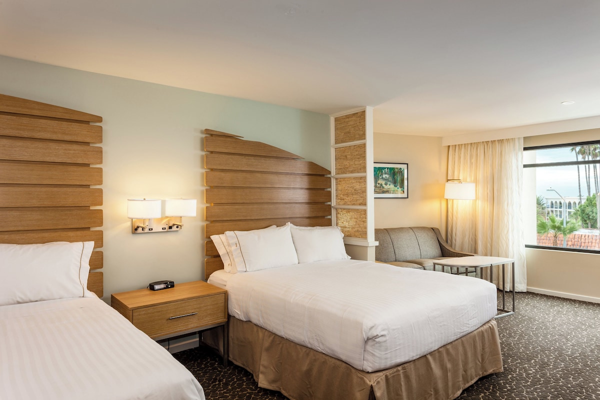 Une chambre d’hôtel avec deux lits, un bureau, une chaise, une lampe et une fenêtre donnant sur un beau paysage.