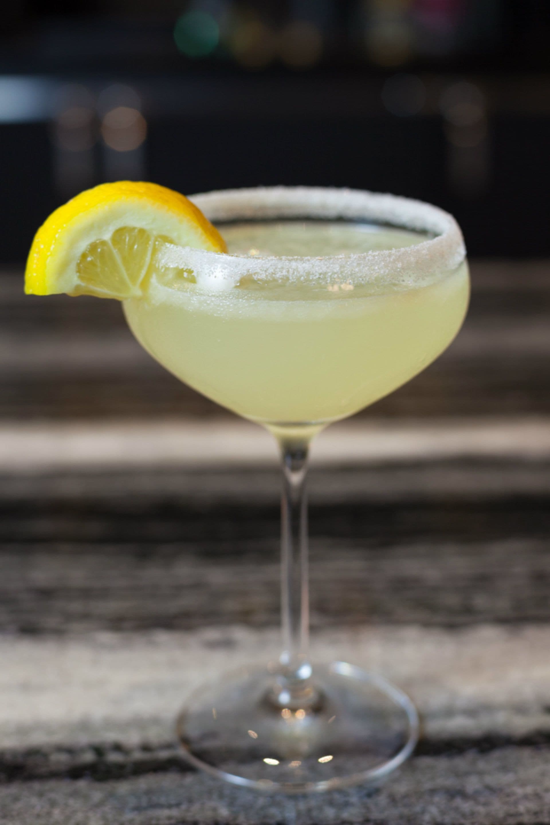 A cocktail in a stemmed glass with a lemon garnish.
