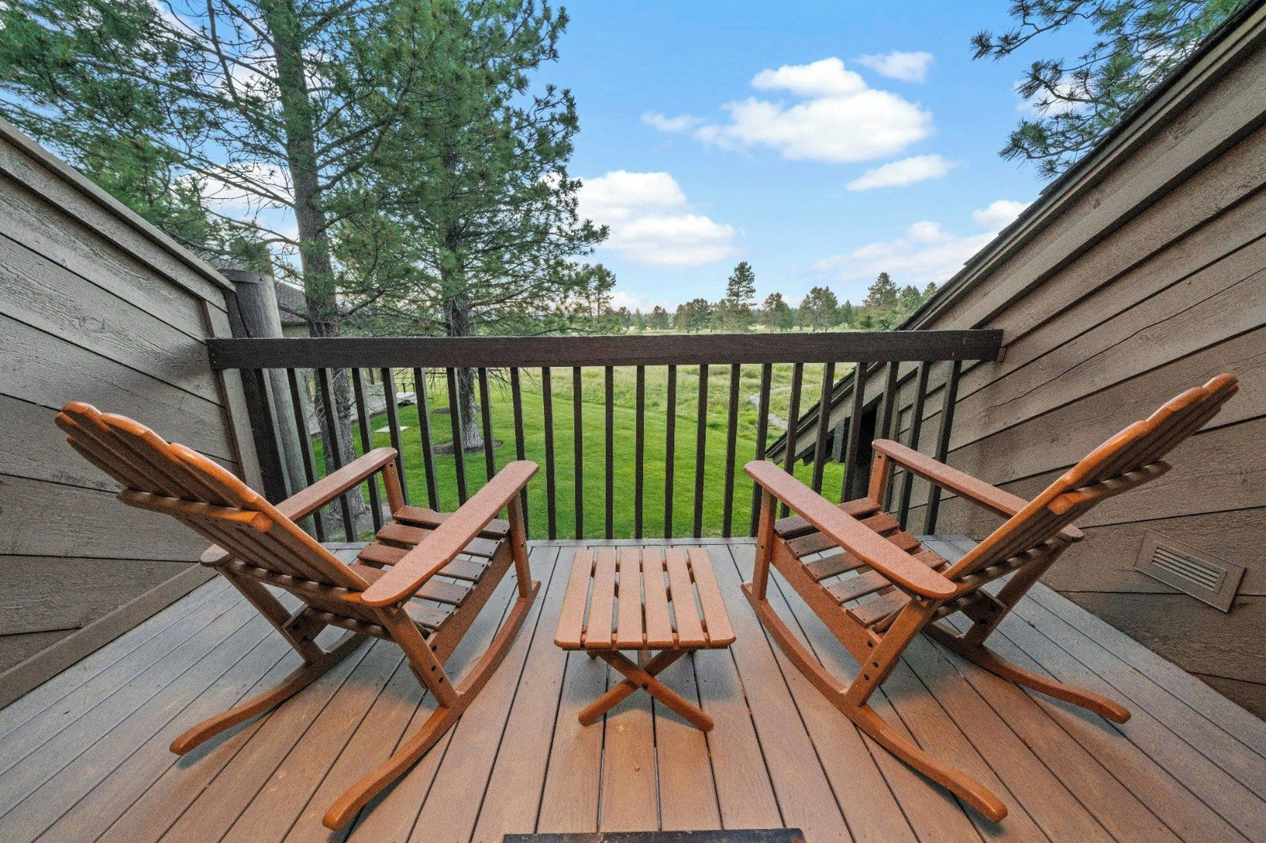 A wooden deck with two rocking chairs and a table, overlooking a grassy yard.