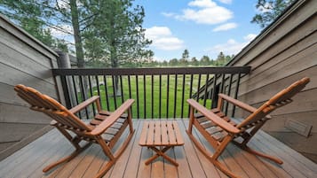 A wooden deck with two rocking chairs and a table, overlooking a grassy yard.
