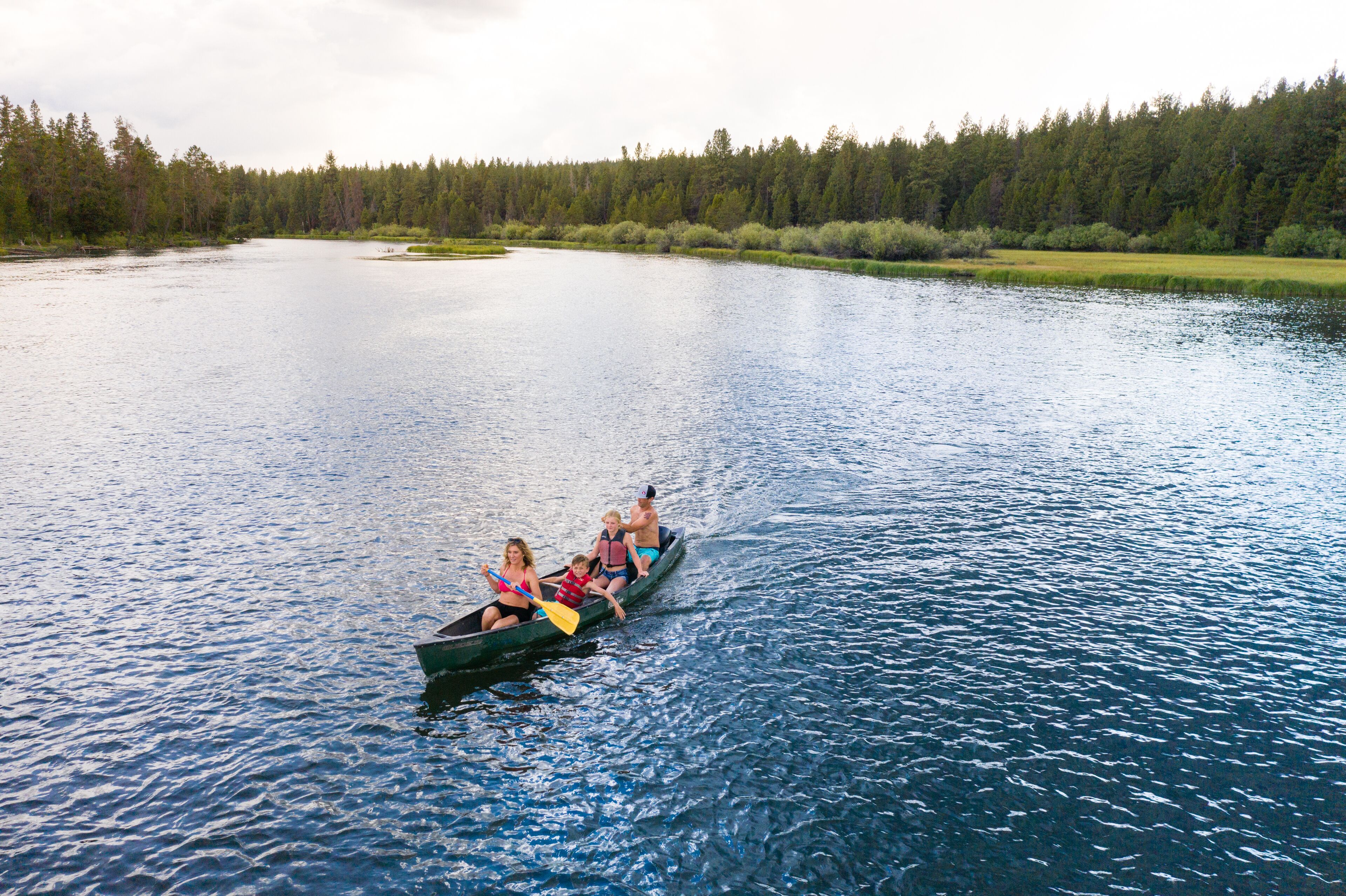 A canoe with four people on a calm river surrounded by dense forest.