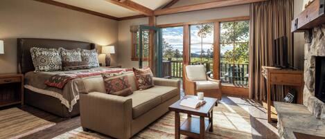 A bedroom with a large bed, a sofa, a small table, and a view of the outdoors through a window.