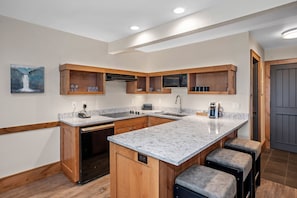 A modern kitchen with wooden cabinetry, a large island with bar stools, a built-in microwave, and a painting on the wall.