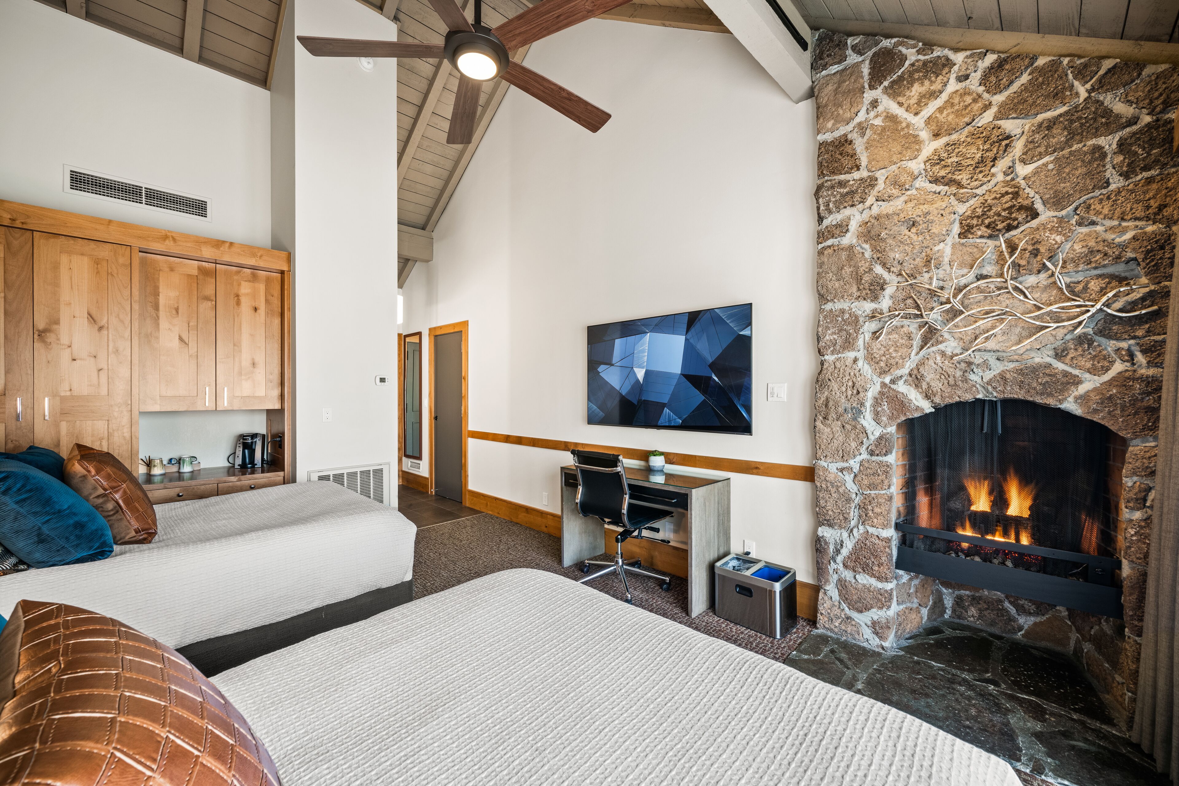 Una habitación acogedora con chimenea de piedra, una cama, un escritorio con silla y un televisor en la pared.