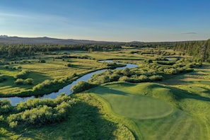 A golf course with a water body, surrounded by dense forests and hills.