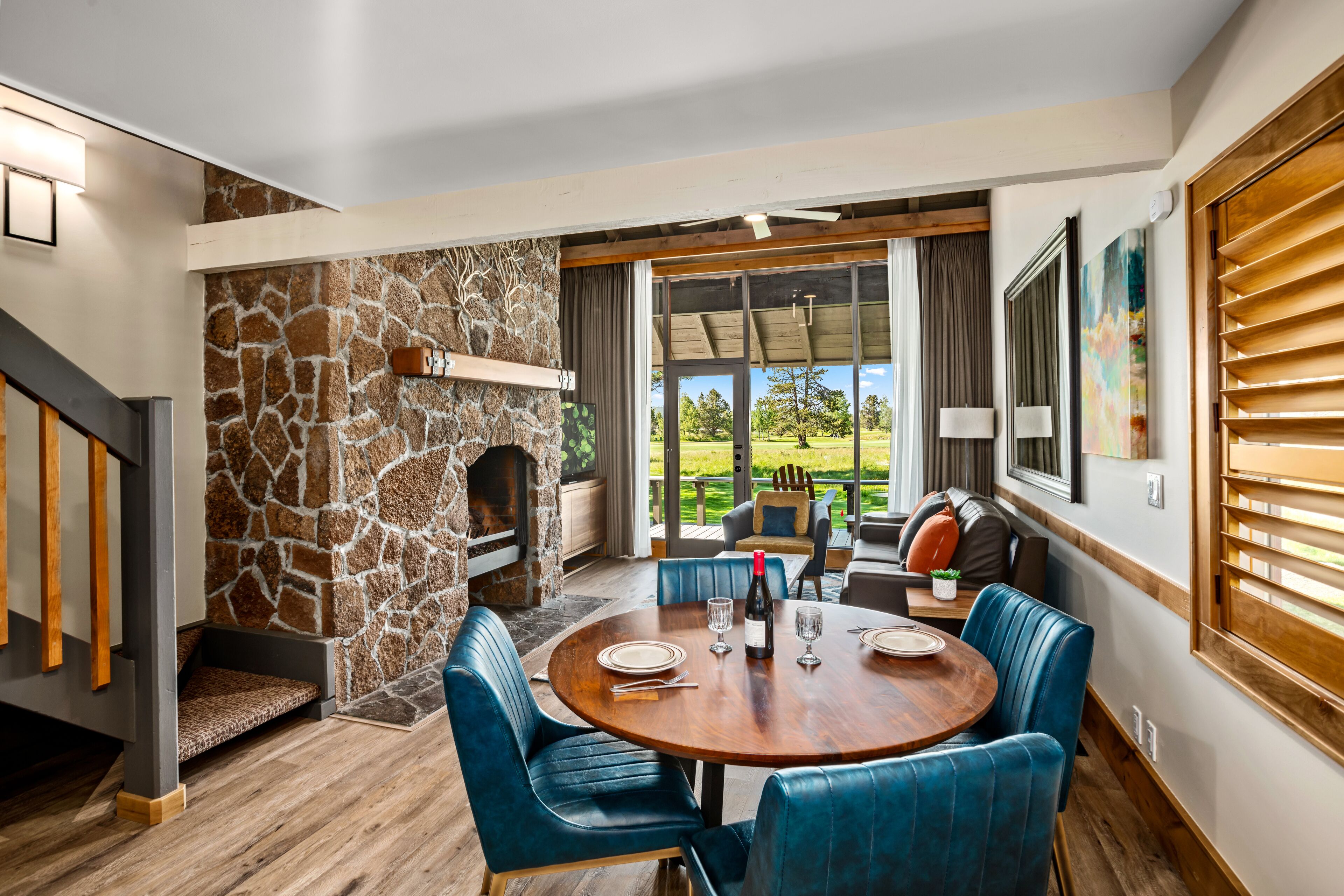 A dining area with a stone fireplace, blue upholstered chairs, and a view of the outdoors.