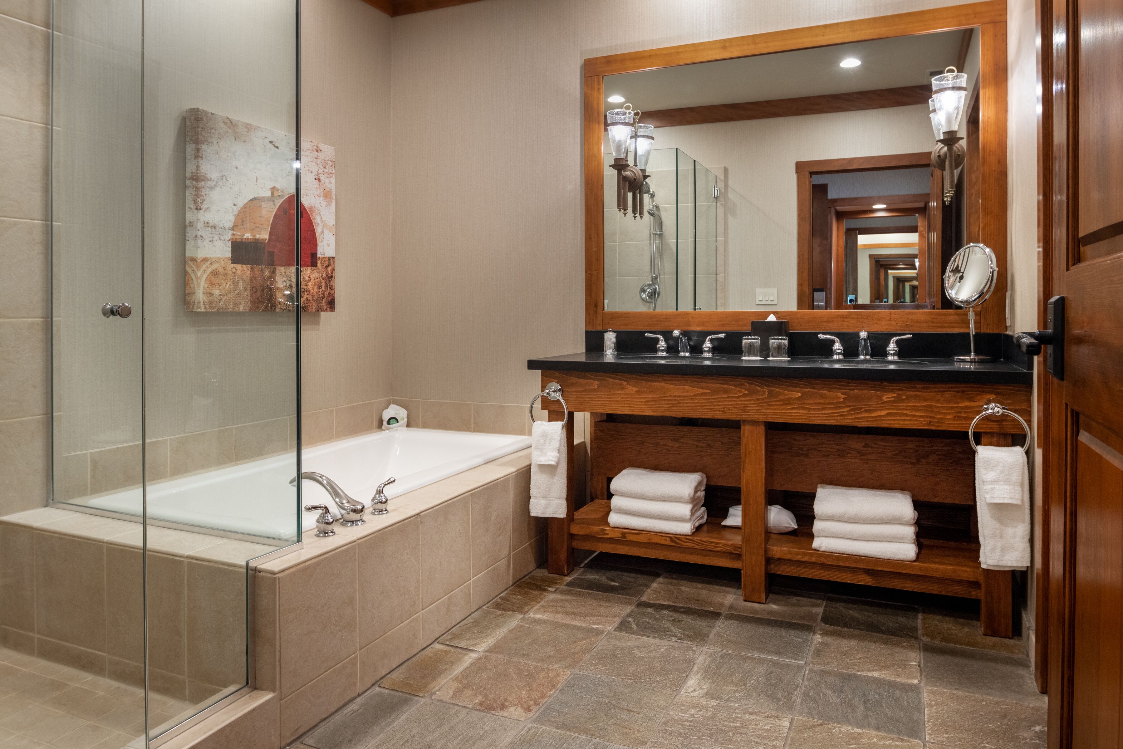 A modern bathroom with a glass-enclosed shower, a freestanding bathtub, a wooden vanity with a large mirror, and neatly folded towels.