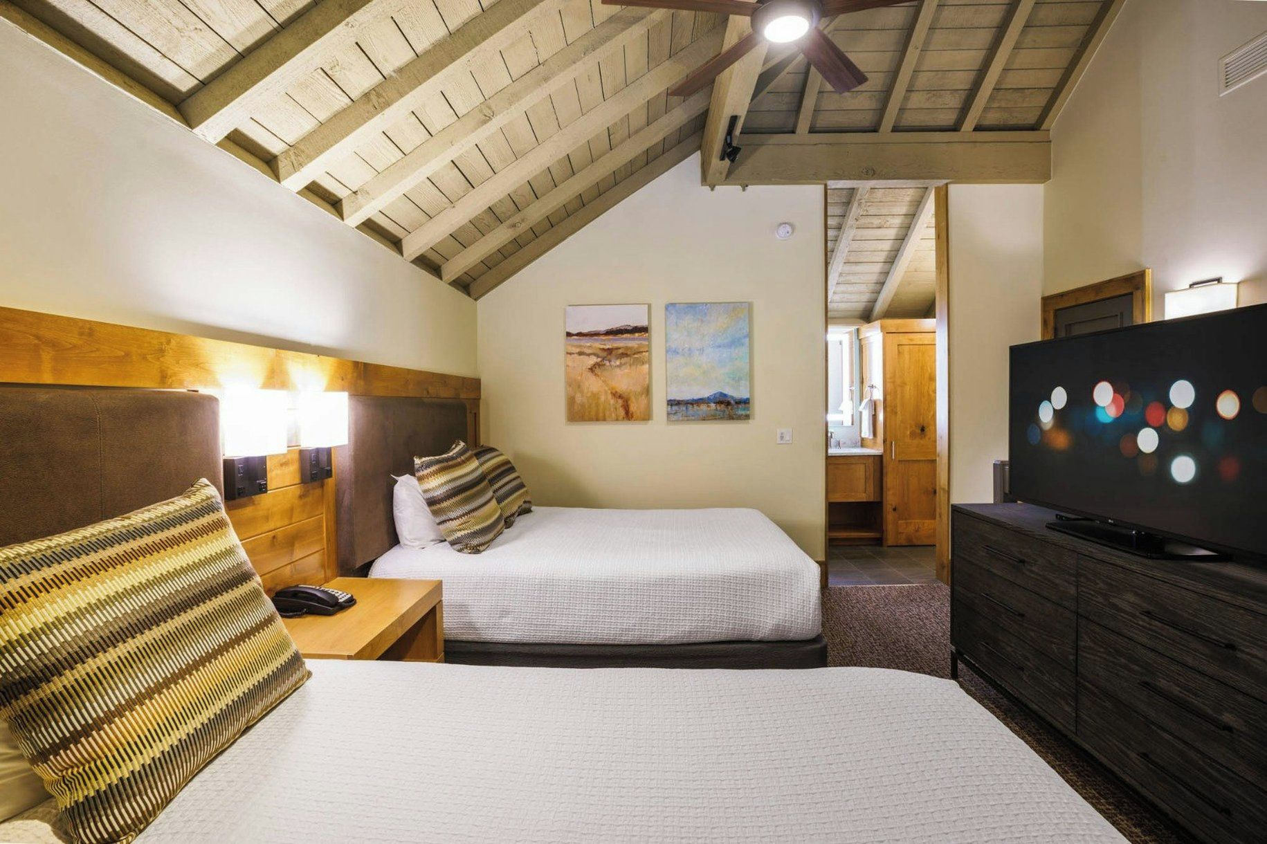 A hotel room with two beds, a television, and artwork on the walls.