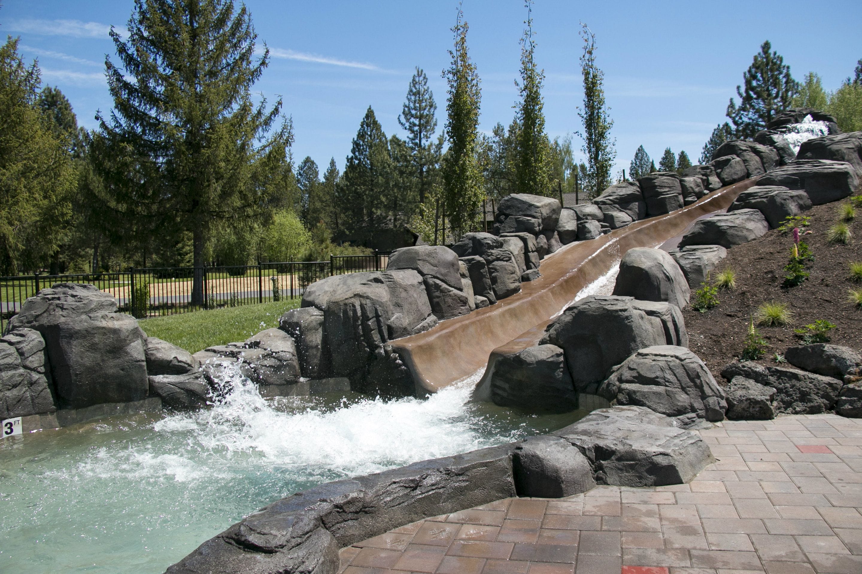 A water slide with a rocky landscape and trees in the background.
