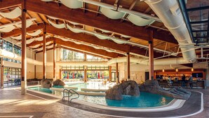 An indoor swimming pool with a waterfall feature, wooden beams, and a bar area.