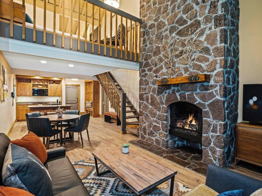 A modern living room with a stone fireplace, a dining area, and a kitchen in the background.