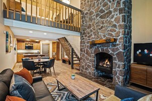 Una sala de estar moderna con chimenea de piedra, un comedor y una cocina al fondo.