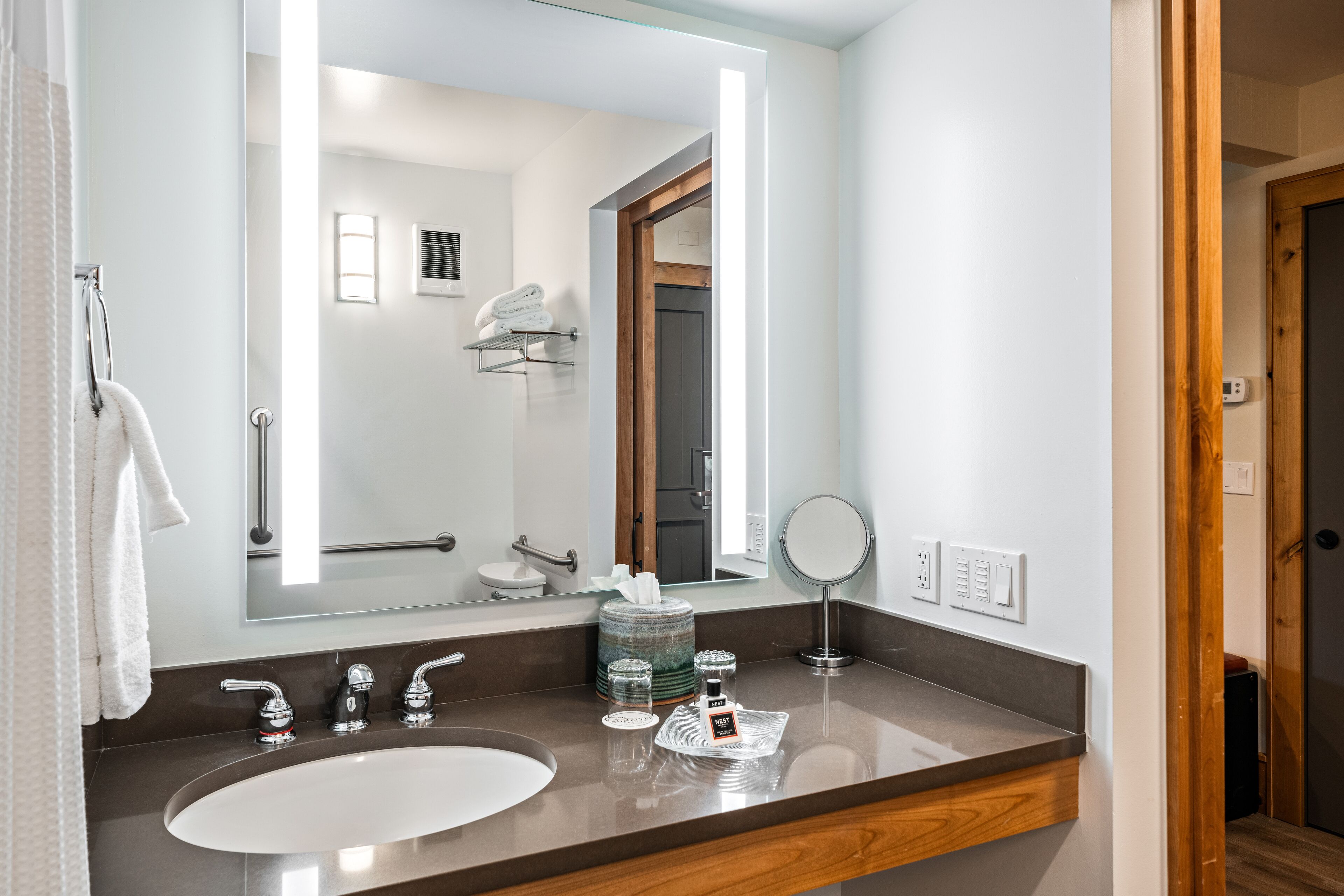 A modern bathroom with a large mirror, a sink, and a shower area visible through the doorway.