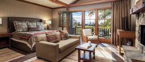 Un dormitorio con cama, sofá, mesa de centro, chimenea y balcón con vistas.