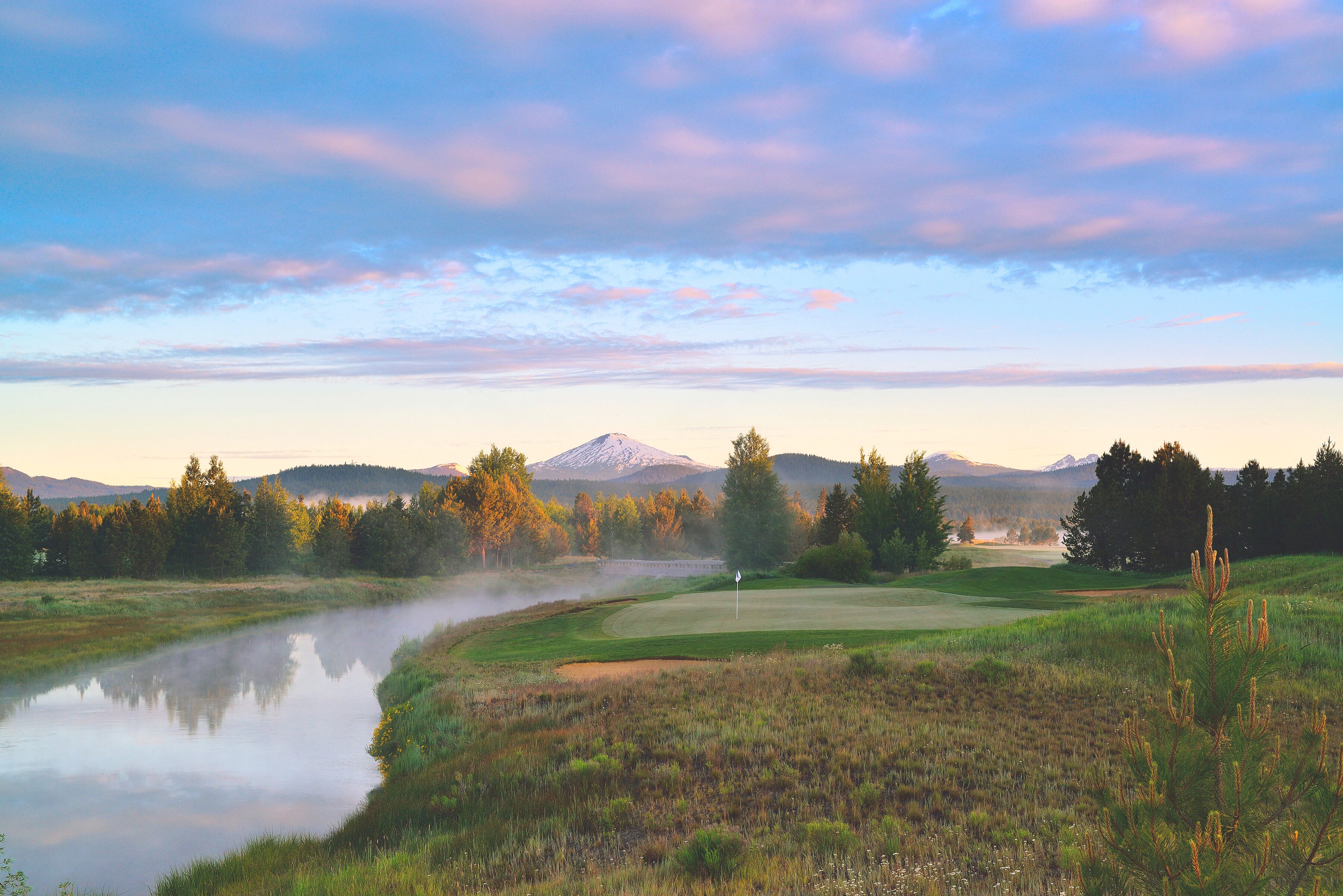 Un campo de golf con un cuerpo de agua, árboles y una montaña al fondo.
