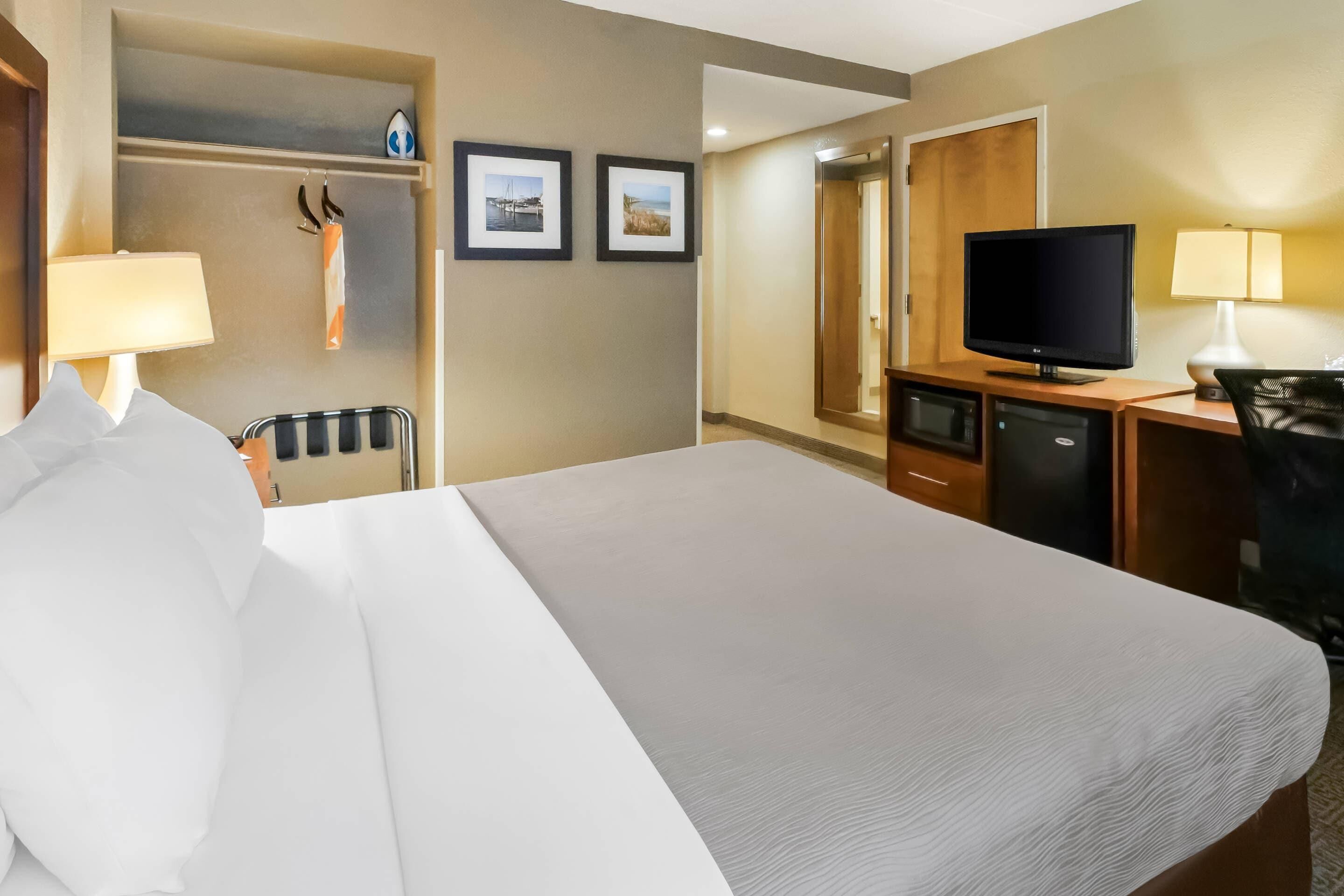Ein Hotelzimmer mit Bett, Schreibtisch mit Fernseher, Kleiderschrank und Spiegel.