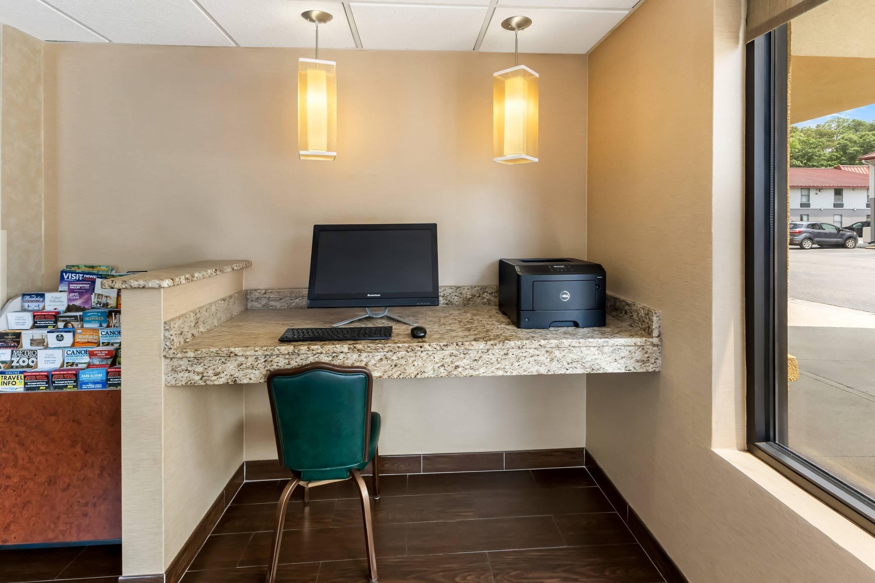 A corner desk with a computer, keyboard, and mouse, a green chair, and a wall-mounted shelf with brochures.