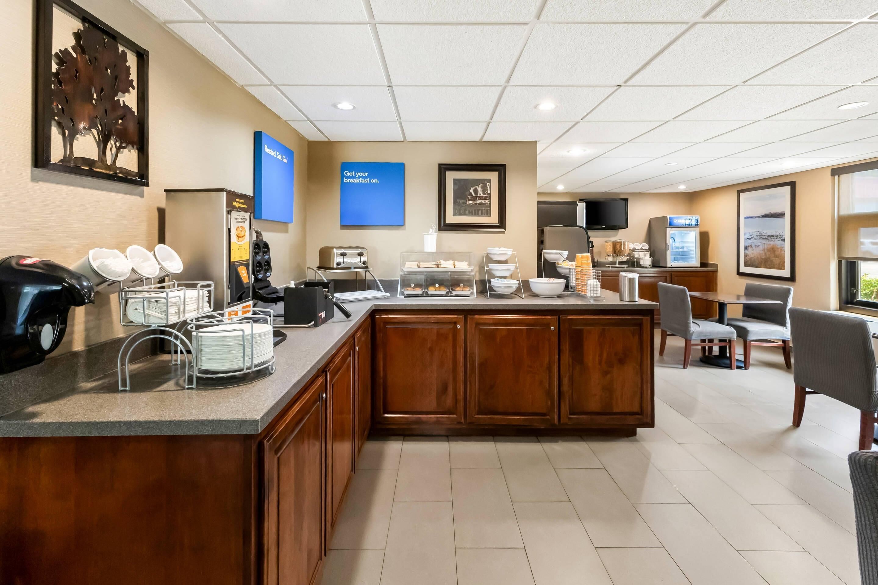 A hotel breakfast area with a central counter, seating, and a refrigerator.