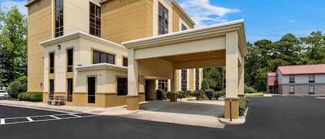 A hotel with a covered entrance, multiple windows, and a parking lot.
