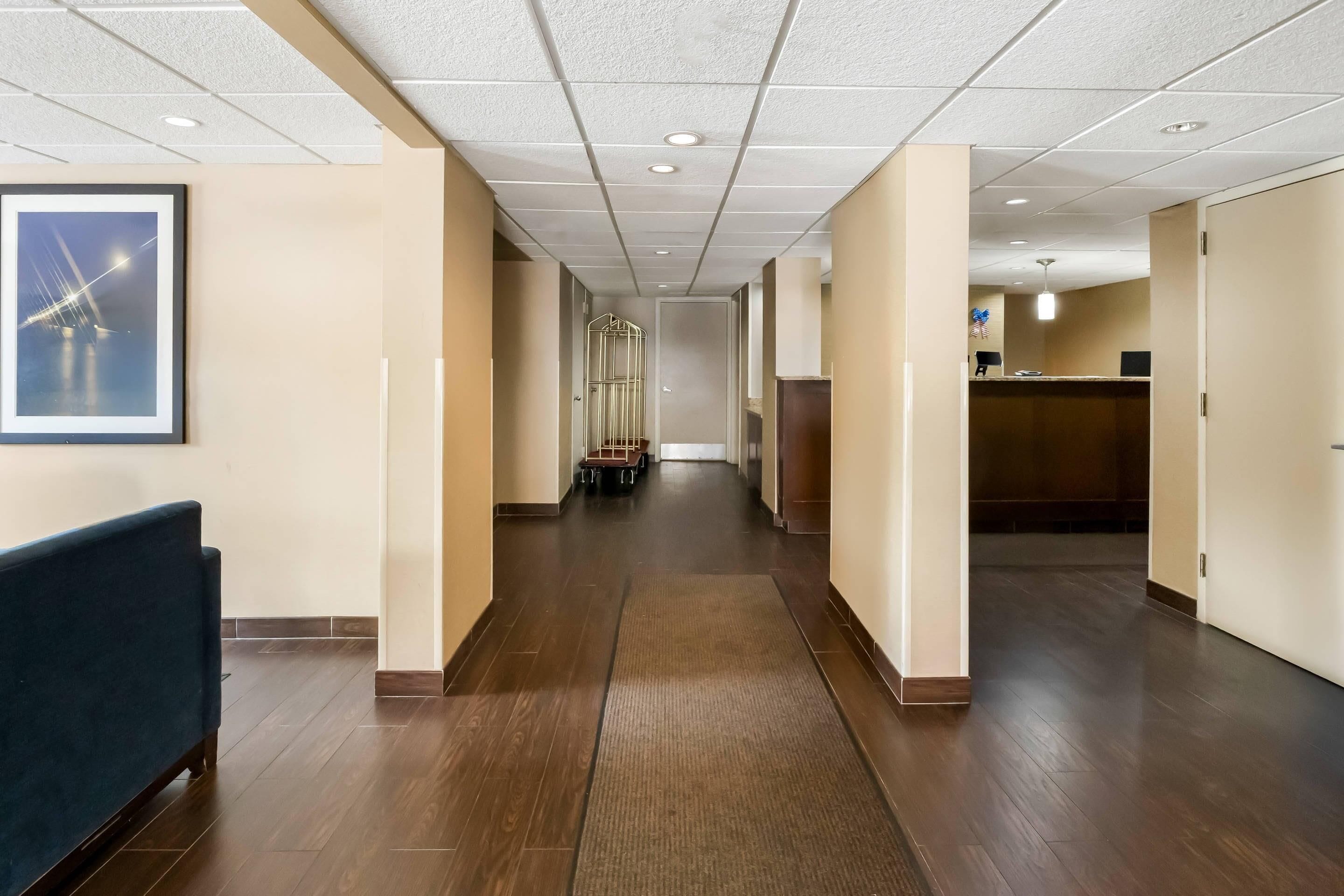 Un couloir d’hôtel avec un comptoir d’accueil, un espace salon et un tableau encadré au mur.