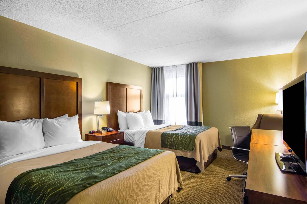 Une chambre d’hôtel avec deux lits, un bureau, une télévision et une fenêtre avec des rideaux.
