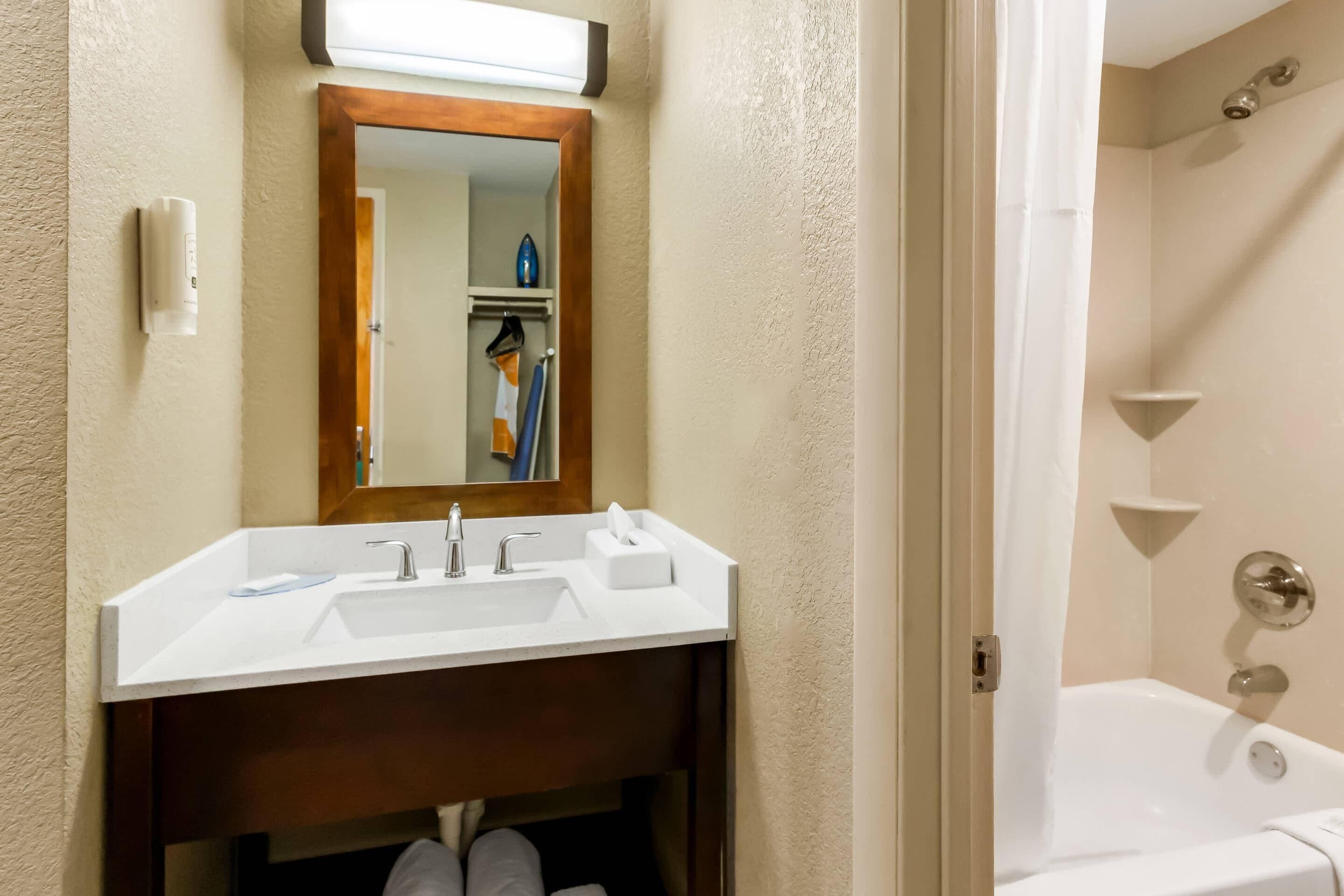 Un baño con un lavamanos blanco, un espejo con marco de madera y una zona de ducha.