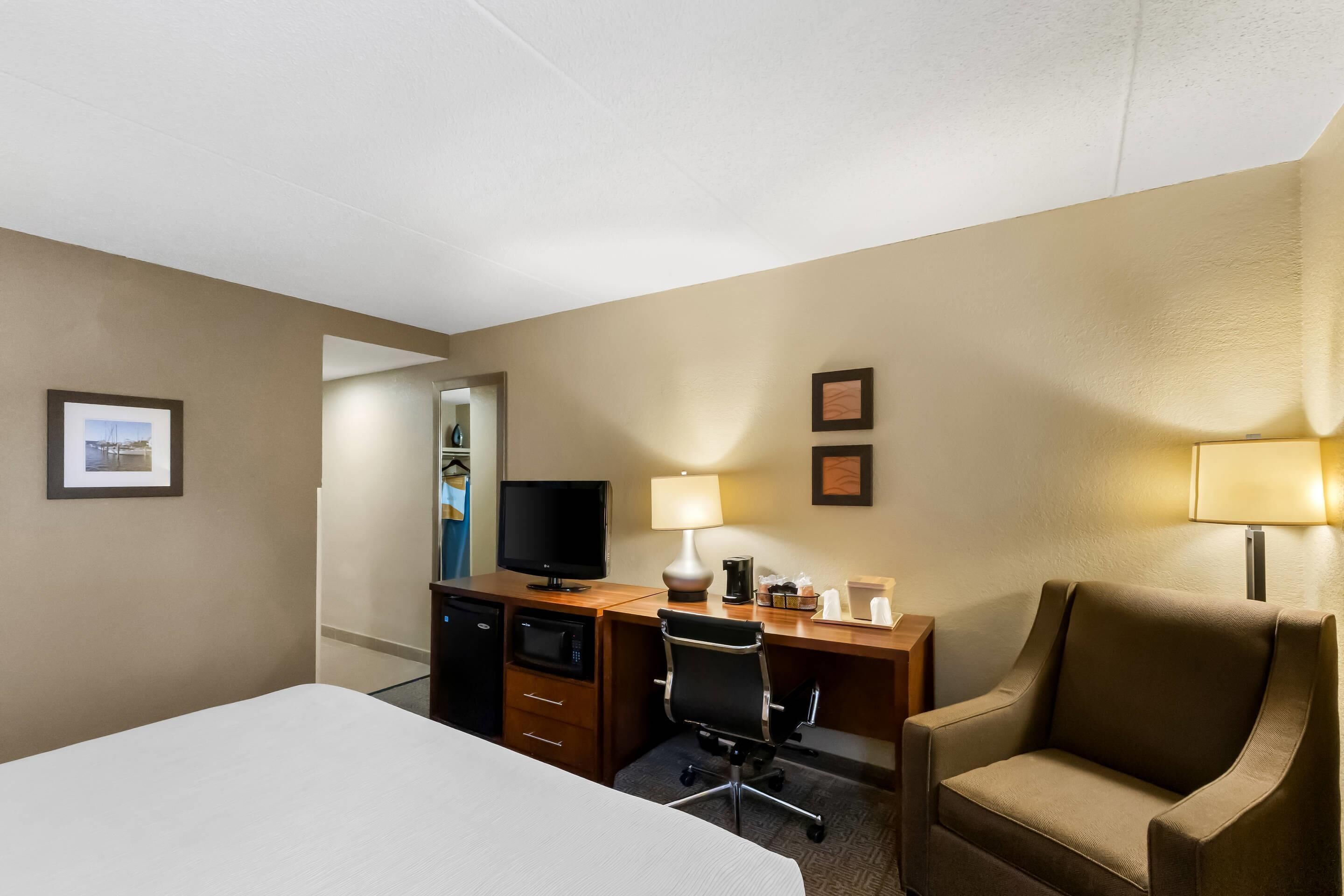 A hotel room with a bed, desk, chair, television, and a lamp.