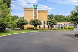 A Quality Inn hotel with a beige facade, a green sign, and a parking lot. - Quality Inn (Newport News)