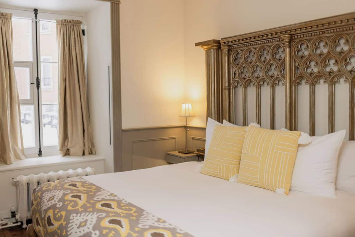A hotel room with a large bed, a nightstand, a lamp, and a window with curtains.
