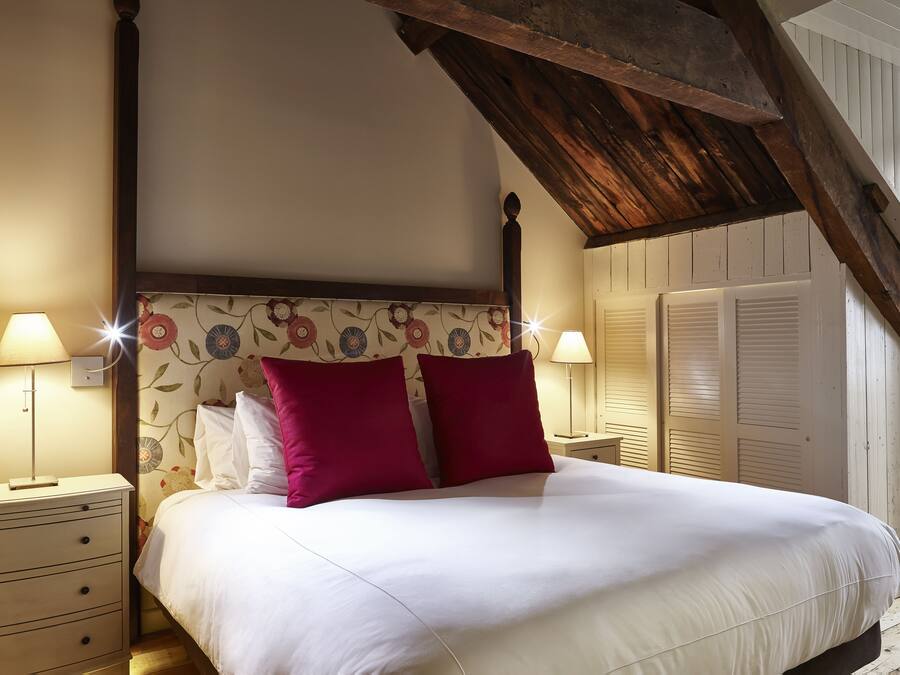 Ett sovrum med en himmelssäng, två sänglampor, ett träpanelat tak och blommig tapet.