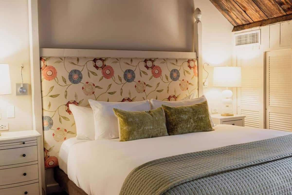 A neatly made bed with white linens and two green pillows, a floral-patterned headboard, and a bedside lamp on a nightstand.