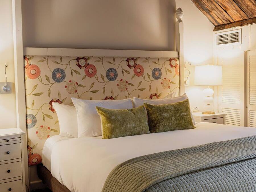 A neatly made bed with white linens and two green pillows, a floral-patterned headboard, and a bedside lamp on a nightstand.