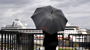 A person holding a black umbrella with "SAINT-ANTONINE" written on it, overlooking a cruise ship docked at a port.