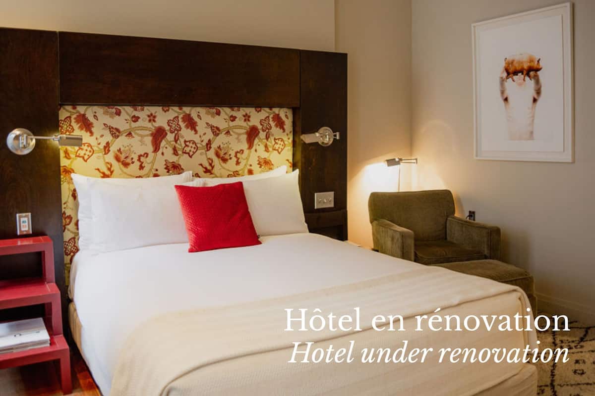 A hotel room under renovation with a bed, a nightstand, a chair, and a wall with a floral pattern.