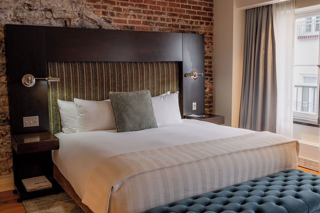 Habitación de hotel con una cama grande, cabecera oscura, cortinas a rayas y vistas a un edificio a través de la ventana.