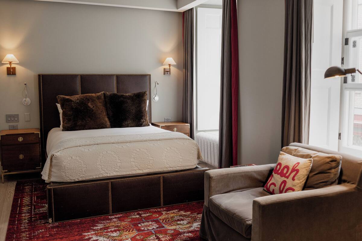 A neatly arranged bedroom with a large bed, bedside lamps, a chair, and a patterned rug.