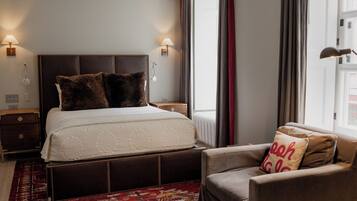 A neatly arranged bedroom with a large bed, bedside lamps, a chair, and a patterned rug.