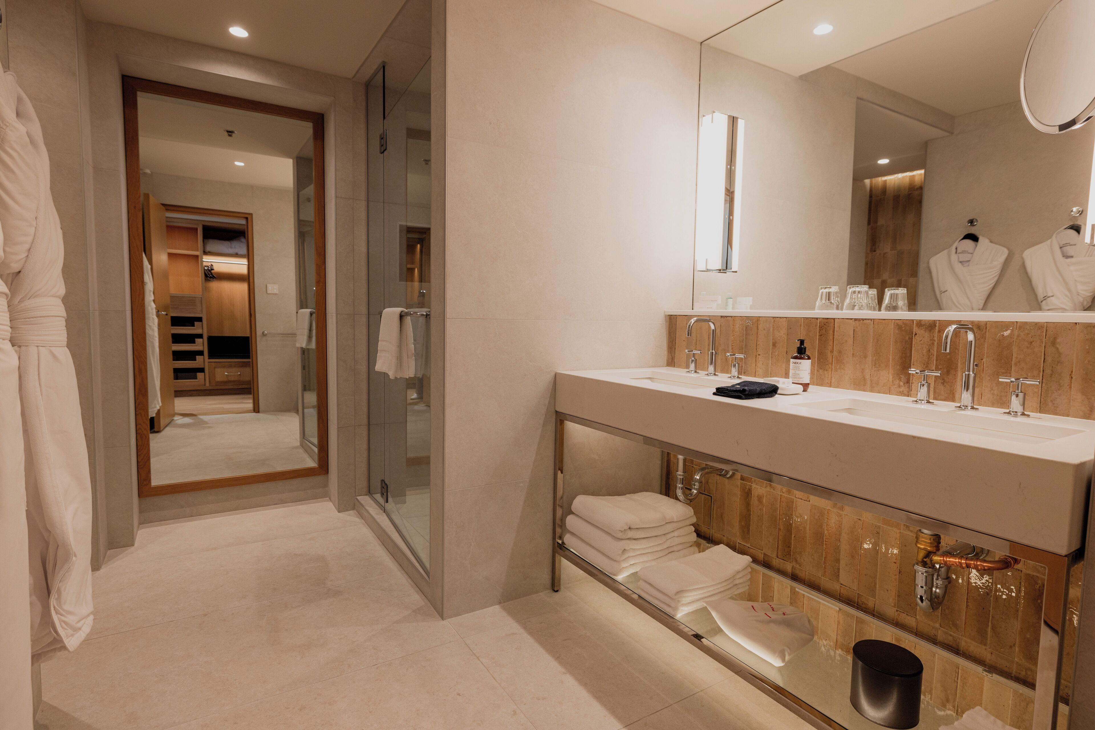 A modern bathroom with a large mirror, dual sinks, and a glass shower enclosure.