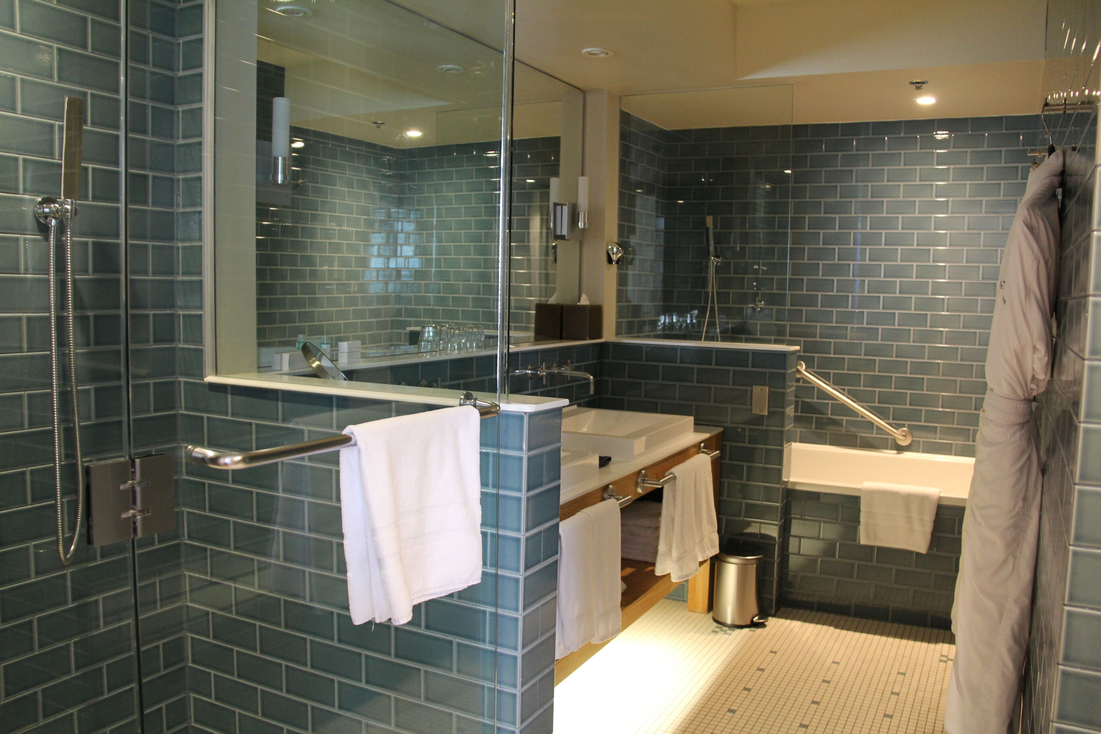 Une salle de bain moderne avec une douche à parois de verre, un grand miroir, un lavabo avec un porte-serviettes et une baignoire.