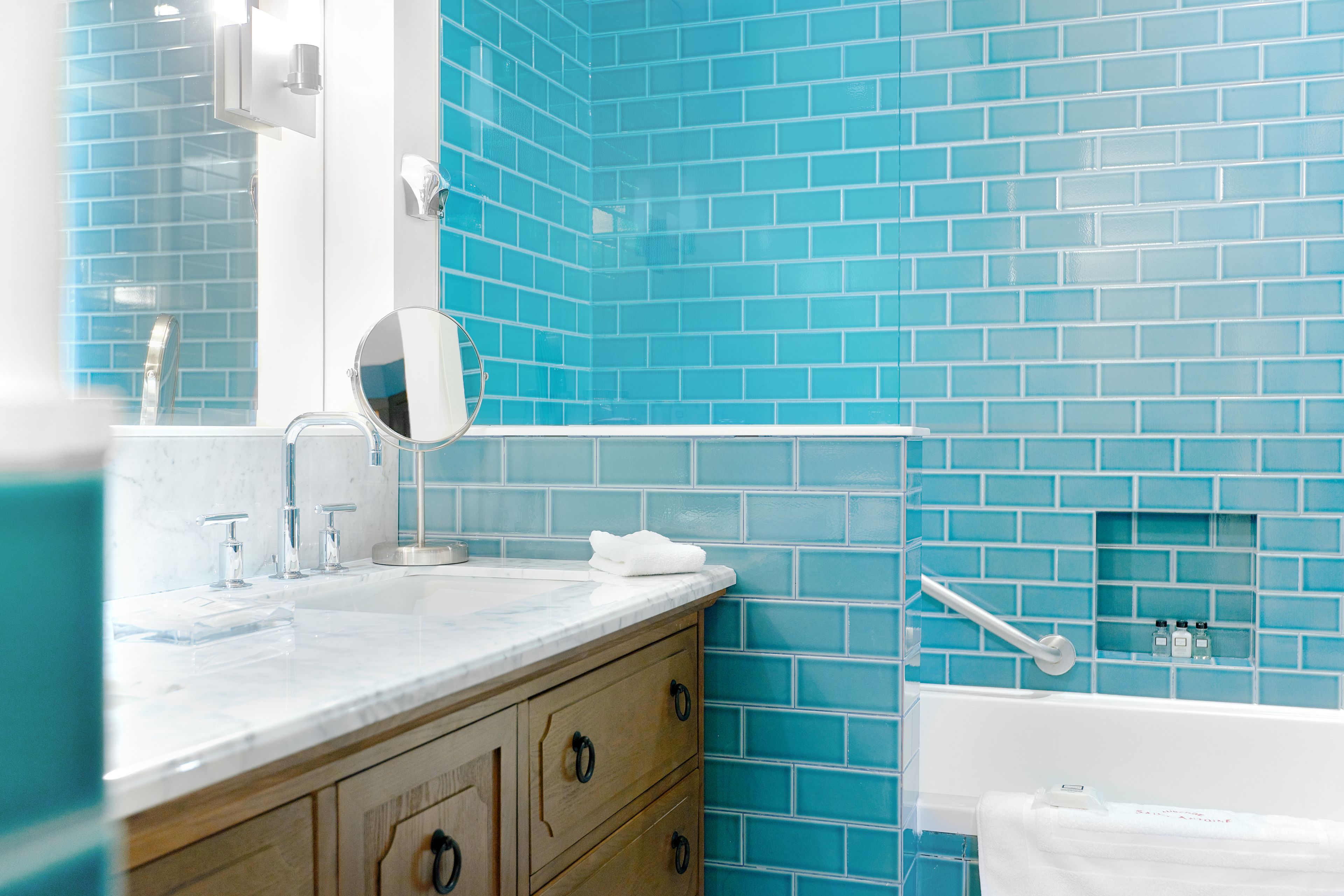 A bathroom with a blue-tiled wall, a white sink with a mirror, and a white bathtub.