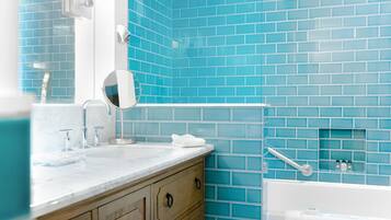A bathroom with a blue-tiled wall, a white sink with a mirror, and a white bathtub.