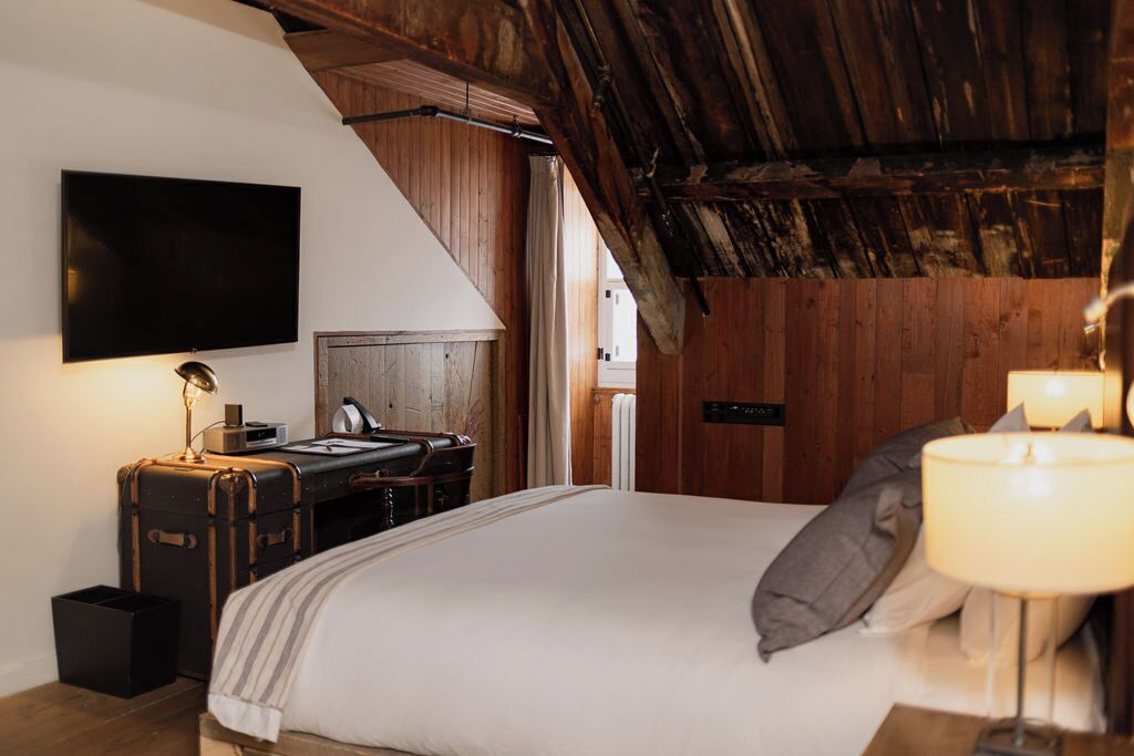 Un dormitorio con cama, escritorio, silla, televisión montada en la pared y techo de madera.