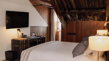 Un dormitorio con cama, escritorio, silla, televisión montada en la pared y techo de madera.