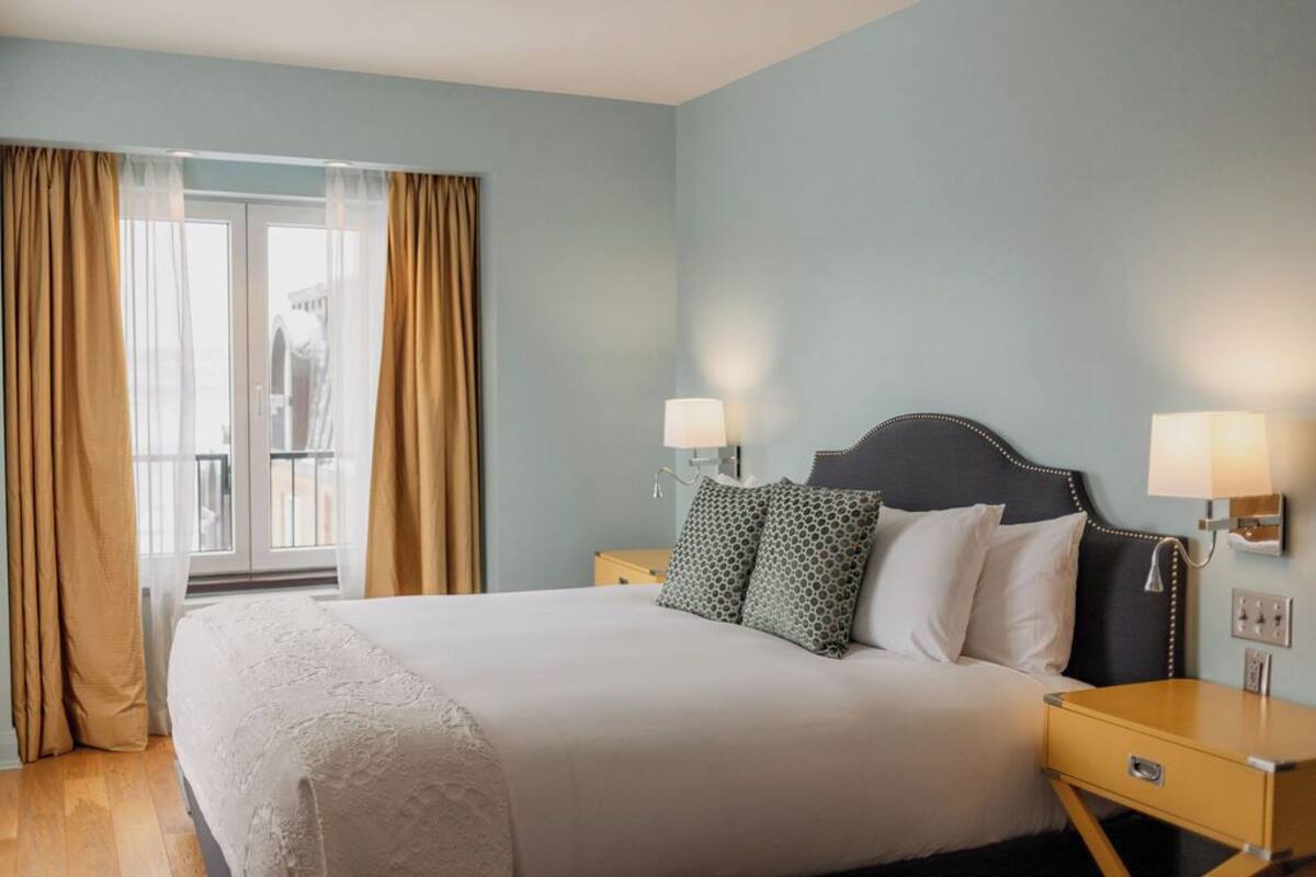 A hotel room with a large bed, two bedside tables, and a window with curtains.